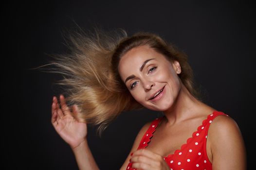 Studio shot of a beautiful Caucasian middle aged woman with perfect natural makeup and flying shiny blond hair, smiling posing against black background with copy space for ads