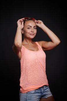 Attractive blonde Caucasian woman with tanned skin and beautiful fit body holding her hands near her face and confidently looking at camera against black background with copy ad space