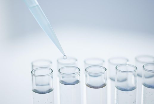 Closeup shot of a dropper being used to fill test tubes in a lab.