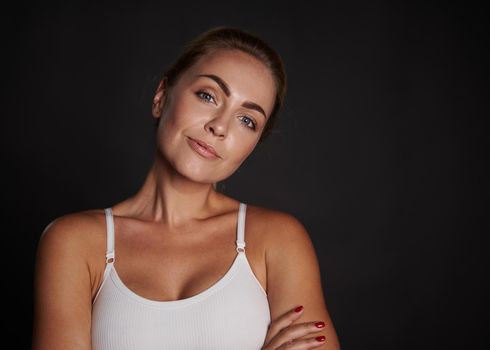 Close-up beauty portrait of a beautiful attractive charming middle aged Caucasian woman in white top smiles looking at camera isolated over black background with copy ad space