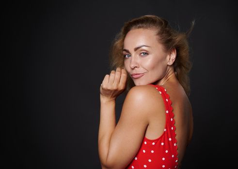 Attractive European woman with healthy clean fresh glowing tanned skin and blond shiny straight hair, natural makeup, wearing red swimsuit with white polka dots isolated on black background