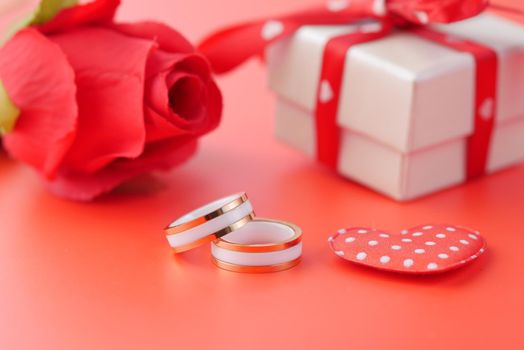 wedding ring and gift box and rose flower on red .