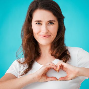 Studio portrait of an attractive young woman making a heart shape over her chest against a blue background.