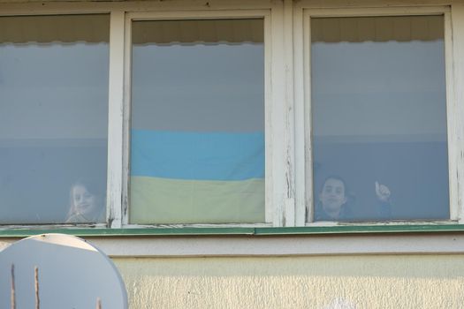 Child at the window with the flag of ukraine. State support in war. Save Ukraine concept.
