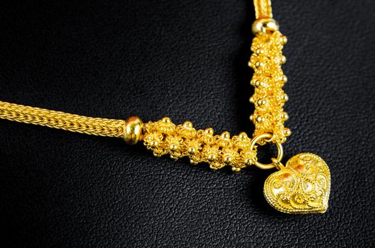 The Gold necklace and heart shape pendant on black leather.