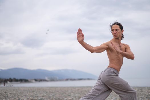 Caucasian man with naked torso practicing wushu on the seashore