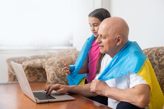 Grandfather and granddaughter with laptop and flag of Ukraine.