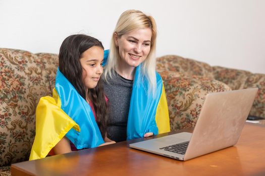 Online Digital Media Support For Ukraine. Freedom And Patriotism Concept. mother and daughter with laptop and ukraine flag.