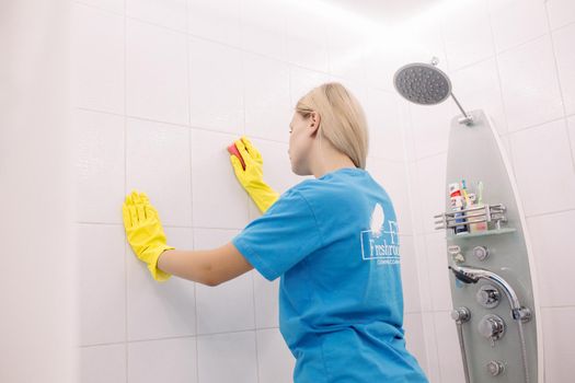 Belarus Minsk 06 29 2018 :Blonde woman, employee cleaning company, wearing in yellow protective rubber gloves, with special cleaning sponge, Housework and housekeeping concept.
