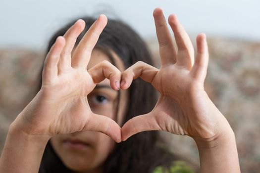 Photo of casual cheerful cute funny girl showing heart shape sign with fingers above her head.