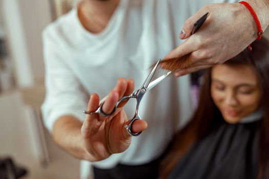 Hairdresser holding scissors in his hands and cutting client hair. Beauty salon services concept