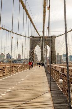 People cycling and walking on Brooklyn Bridge New York City in the evening, wire ropes in the forefront, Skyline in the background, vertical