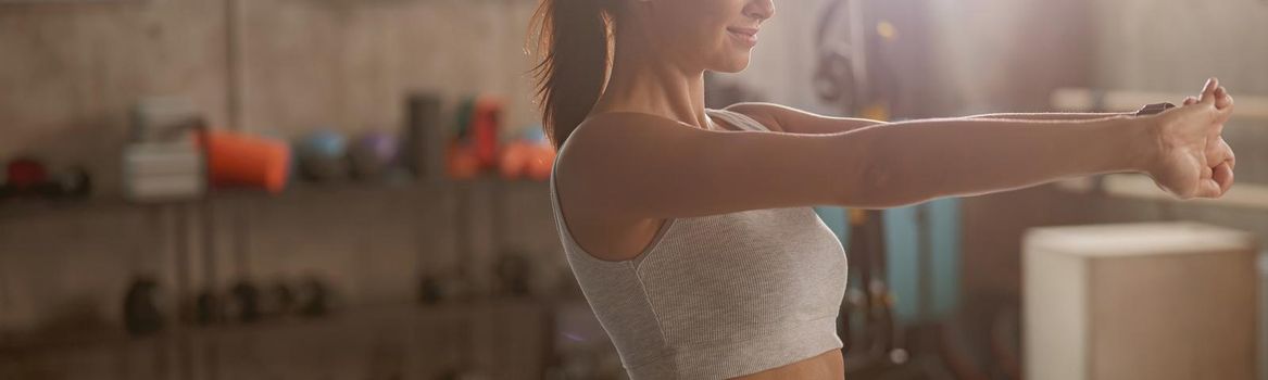 Slender athletic woman in sports top doing stretching and getting ready for workout in the fitness club