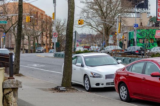 Cars parked on a street next to a sidewalk, Traffic at Staten Island near the Ferry Terminal, New York City, during winter day with overcast and traffic lights in the background, horizontal