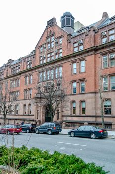 The Gottesman Libraries Building Facade with cars parked in forefront, New York City, during winter day with overcast, Plants and trees in front, vertical