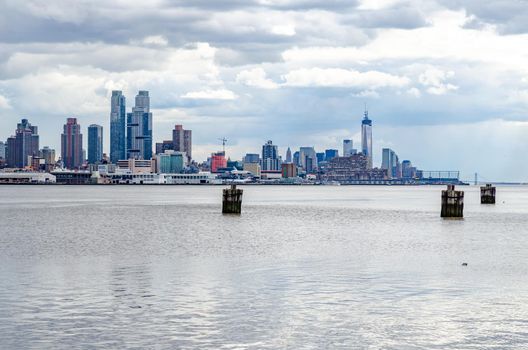 View of One World Trade Center construction site with Hudson River and wooden boat deck in front, New York City during cloudy winter day, horizontal