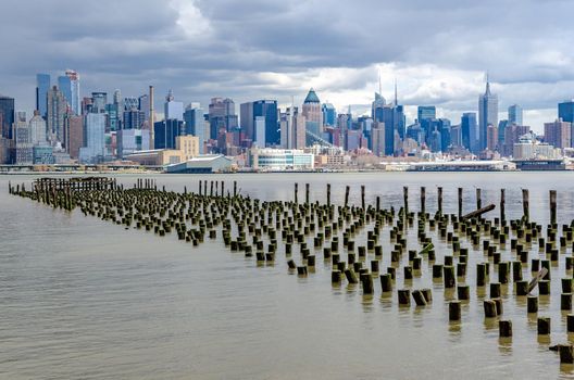 View of Manhattan Skyline, New York City with Hudson river and old wooden landing stage in front during cloudy winter day, vertical
