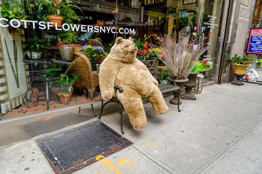 Huge brown Teddy Bear sitting on a bench in front of Scotts Flowers New York City retail store, horizontal
