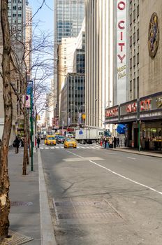 Radio City Music Hall, New York City with street and sidewalk in the forefront, lots of traffic, yellow Taxi Cabs, on the street during daytime, vertical