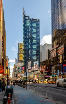 Time Square New York City with skyscraper, lots of advertisement, people walking around, traffic and yellow Taxi Cabs, low angle view during sunset, vertical