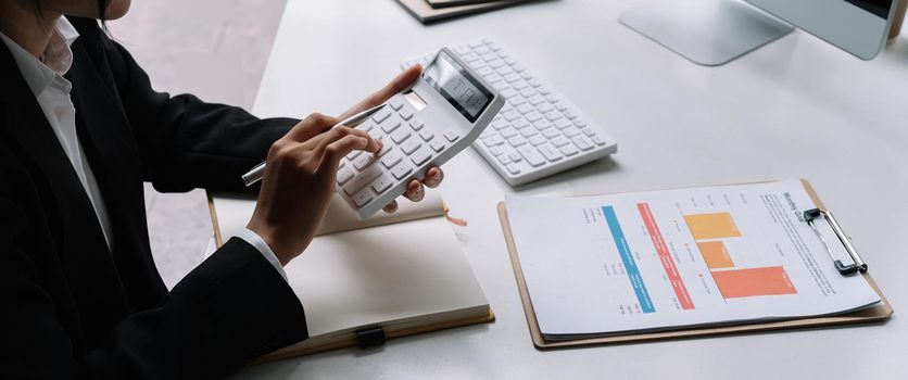 Close up of businessman or accountant hand holding pen working on calculator to calculate business data, accountancy document and laptop computer at office, business concept.