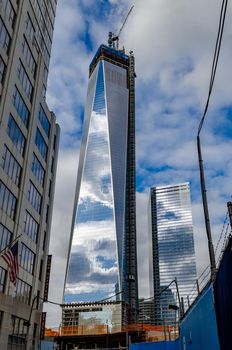 One World Trade Center construction area with  clouds reflection in the window, crane on top during daytime with overcast, New York City, view from low angle, vertical