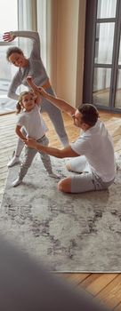 Top view of happy father and mother teaching their little daughter exercising in light living room