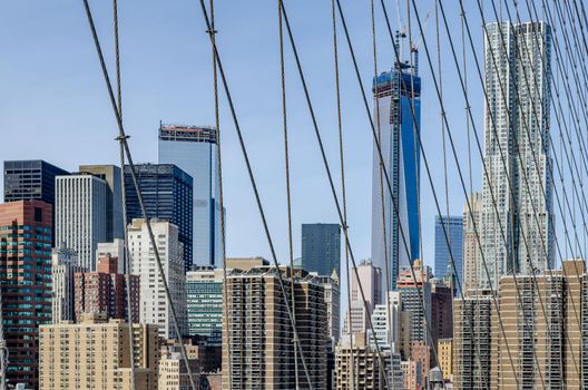 Skyline of Manhattan with one World Trade Center in Construction, during daytime with clear sky with wire ropes of Brooklyn Bridge in the forefront, horizontal