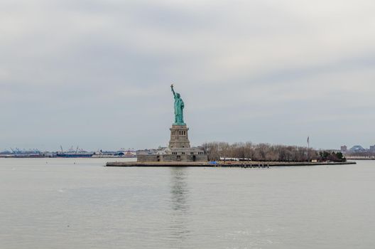 Statue of Liberty National Park, New York City, during winter day with overcast, waves and reflection of the statue on the water, horizontal