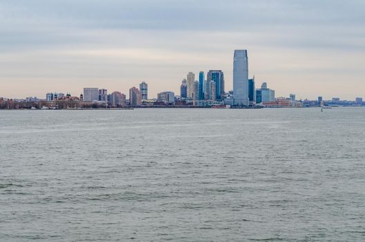 Jersey City, New Jersey with office building skyscraper, Hudson river in forefront, during winter evening with overcast, horizontal