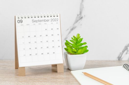 The September 2022 desk calendar with plant on wooden table.