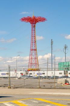 Red Parachute Jump at Luna Park Amusement Park, Coney island, Brooklyn during winter day, view from the distance, with city street and fence in front, New York City during sunny winter day with cloudy sky, vertical