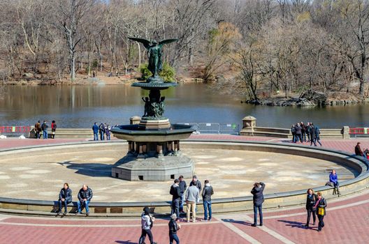 Bethesda Fountain with Angel of the Waters Sculpture with people walking and standing around the fountain, lake in the background Central Park New York during winter, horizontal