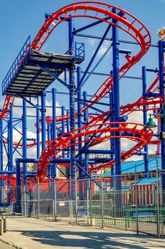 Soarin' Eagle Rollercoaster red and blue colored, close-up at Luna Park Amusement Park, Coney island, Brooklyn, New York City during winter day with clear sky, view from low angle with fence in front, vertical