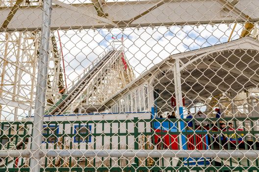 Cyclone Wooden Rollercoaster at Coney island, view of the station and hill, fence in front, Brooklyn Luna Park Amusement Park, New York City during winter day with cloudy sky, horizontal