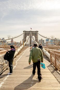 Brooklyn Bridge New York City with a small group of People walking on the Bridge, Man carrying back rear view, in the evening during winter, vertical