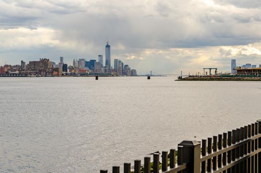 One World Trade Center Construction site with Jersey City, Hudson river and Fence in front in the evening with cloudy sky, horizontal