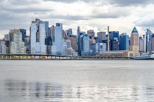 View of Manhattan, New York City Skyline with bridge and Hudson river in front during cloudy winter day, horizontal