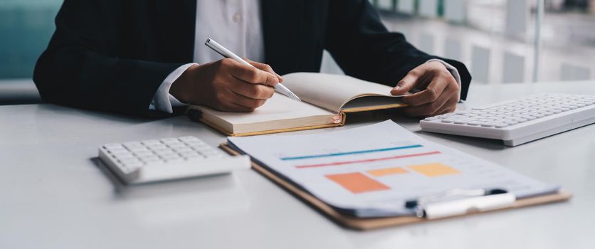 close-up shot of accountant using calculator while taking notes on office desk