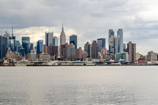 View of Manhattan Skyline, New York City with Empire State Building, Hudson river in front during cloudy winter day, horizontal