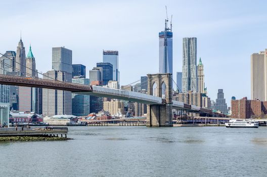 Brooklyn Bridge New York City with construction area on the bridge with Manhattan Skyline and One World Trade Center Construction area in the Background, Hudson river with statue cruises ship in the forefront, daytime with great weather, horizontal