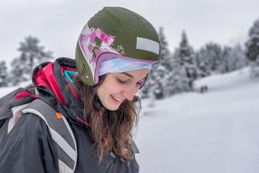 Woman with brown hair wearing ski wear and ski helmet looking down with eyes closed, smiling cheerful, side view, stryn norway, close-up, horizontal