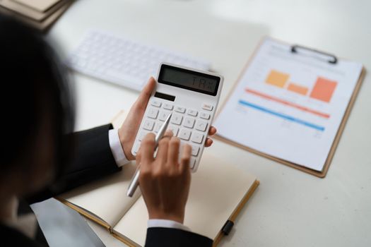 Close up of businessman or accountant hand holding pen working on calculator to calculate business data, accountancy document and laptop computer at office, business concept.