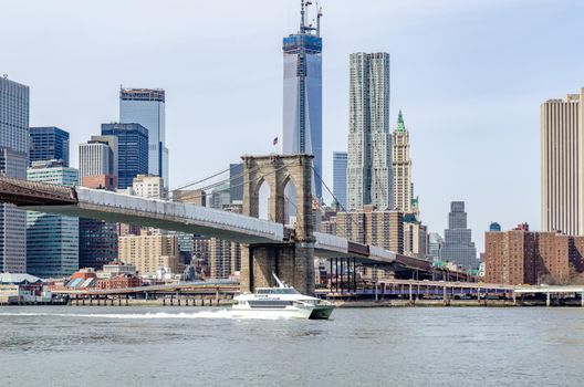Brooklyn Bridge New York City with construction area on the bridge with Manhattan Skyline and One World Trade Center Construction area in the Background, Hudson river with seastreak ship passing by in the forefront, daytime with great weather, horizontal