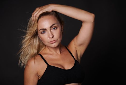 Confident beautiful fitness young Caucasian woman with a healthy toned body, clean glowing tanned skin posing in a black bra against colored background with copy ad space