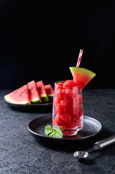 Ripe watermelon noisette balls in glass with mint on dark background. Summer dessert.