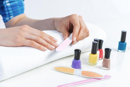 Woman using nail file and create perfect nails shape. Colorful nail polish bottles on table. Grinding female nails with nail file. Woman doing herself nail care procedure at home. Beauty and hygiene