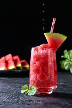 Ripe watermelon noisette balls with sada in glass and falling water drops on dark background. Refreshing summer drink.