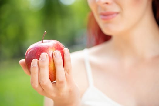 Close-up of the woman's hand with an apple. A young woman is holding an apple and smiling.