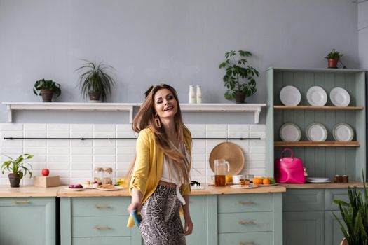 Full length of gorgeous brunette in fashionable clothes and heels dancing in the kitchen. Feeling happy in the morning. Modern interior.